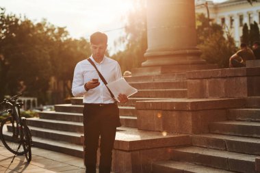 Telefon kullanarak, mesaj atarak. Siyah bisikletli resmi giysili bir işadamı şehirde..
