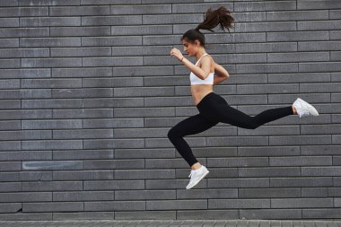 Hızlı koşuyor. Genç, sportif esmer, ince vücutlu, şehirde gündüz vakti tuğla duvara yaslanmış..