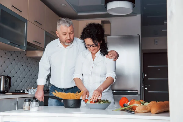 いい人達だ 台所で野菜を使った料理を作る白いシャツを着た男と妻 — ストック写真