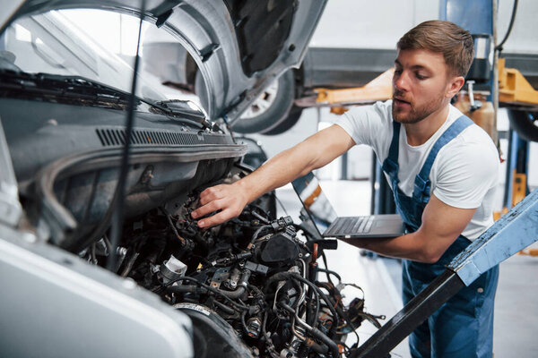 Silver colored laptop in hand. Employee in the blue colored uniform works in the automobile salon.