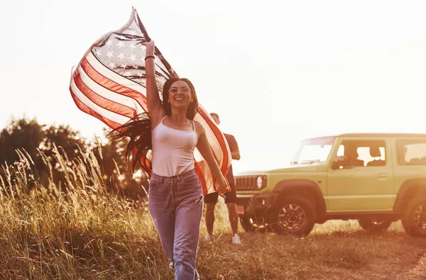 女孩向前跑 朋友们周末过得很愉快 在他们的绿色轿车旁边挂着美国国旗 — 图库照片