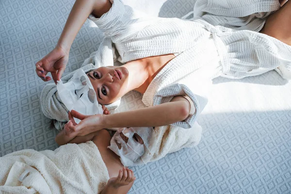 母と娘は顔に美容マスクでスパの日を持っています タオルを頭にベッドに寝そべって — ストック写真