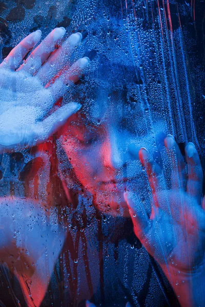 ホット ガール スタジオはネオンで暗いスタジオで撮影しました 濡れたガラスの後ろの美しい女性の肖像 — ストック写真