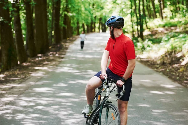 跑在后面 骑自行车的人在森林里的柏油路上 — 图库照片