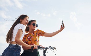 Harika selfie çekiyorum. Bisikletli iki bayan arkadaş gölün yanındaki sahilde eğleniyor..