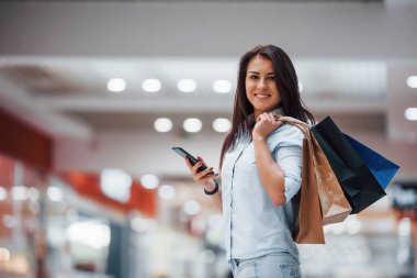 Süpermarkette elinde bir sürü paket ve telefonla esmer bir kadın alışveriş yapıyor..