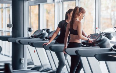 Spor elbiseli iki genç kız koşu bandında spor salonunda beraberler..