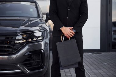 Siyah takım elbiseli ve kravatlı işadamlarının yakın görüntüsü ellerinde alışveriş torbalarıyla modern otomobilin yanında duruyor..