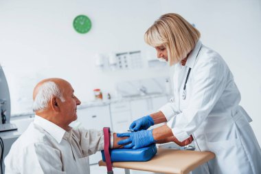 Kadın doktor klinikte yaşlı erkek hastaya iğne yapmaya hazırlanıyor..