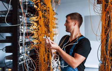 Üniformalı genç adam şaşkın hissediyor ve sunucu odasında internet teçhizatı ve kablolarla çözüm arıyor..