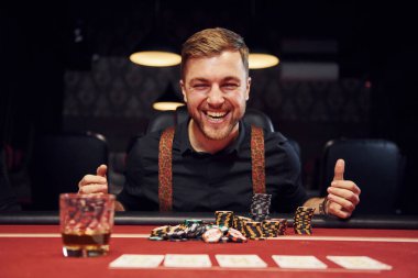 Mutlu zarif genç adam kumarhanede oturuyor ve pokerdeki zaferini kutluyor..