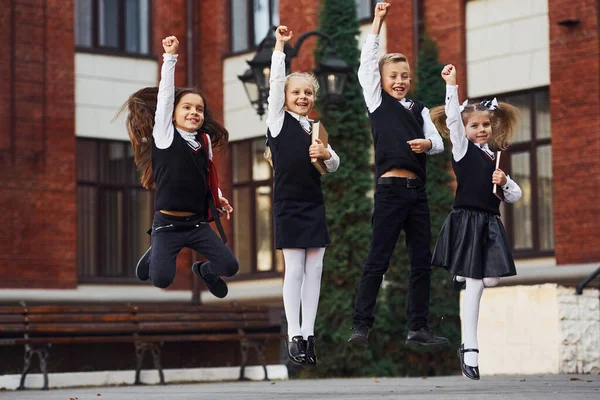 Grupo Crianças Uniforme Escolar Pulando Divertindo Livre Juntos Perto Prédio — Fotografia de Stock