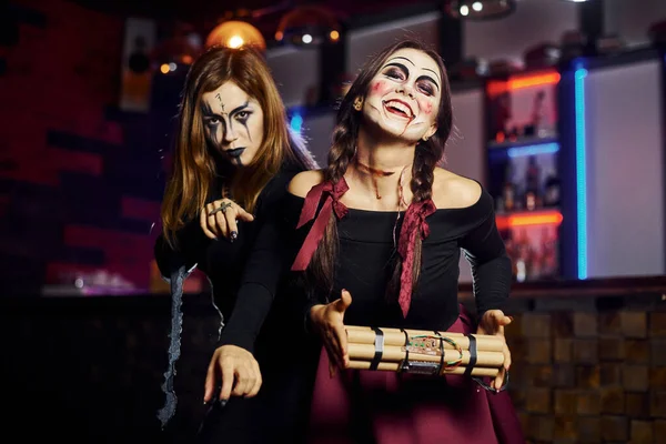 Two female friends is on the thematic halloween party in scary makeup and costumes with time bomb.