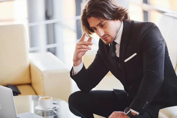 ソファの上に座る 黒のスーツとネクタイでハンサムな若いビジネスマンの肖像 — ストック写真