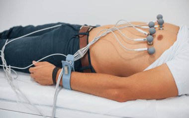 Klinikteki yatakta yatan ve elektrokardiyogram testi yaptıran bir adam..