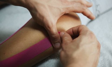 Doktor kadına Kinesio bandıyla bacak tedavisinde yardım eder..