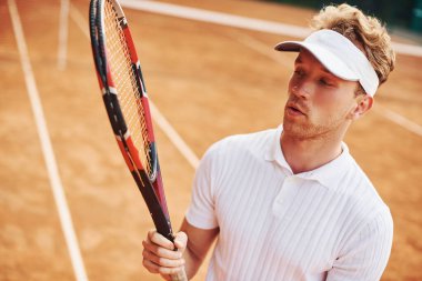 Raketi elinde tutuyor. Spor elbiseli genç tenisçi dışarıda..