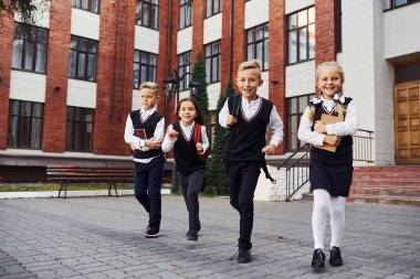 Okul üniformalı bir grup çocuk eğitim binasının yanında kameraya poz veriyor..