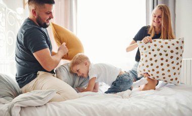 Genç evli çift ve küçük oğulları gündüz yatak odasında yastık savaşı yapıyorlar..