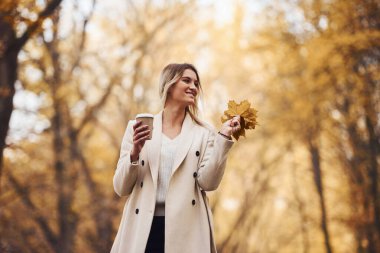Bir bardak içki tutuyor. Gündüz vakti sonbahar ormanındaki genç esmerin portresi..