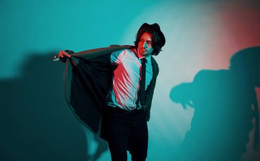 Şapkalı, takım elbiseli ve kravatlı genç bir adamın portresi stüdyodaki neon ışıklarda duruyor..