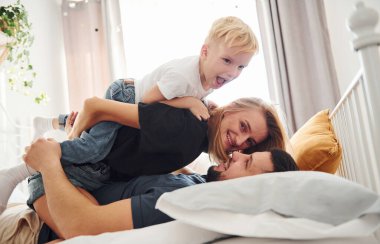 Genç evli çift ve küçük oğulları yatağa uzanıp gündüz vakti yatak odasında eğleniyorlar..