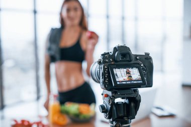 Spor vücutlu bir kadın vlogger 'ı. Sağlıklı yiyeceklerle birlikte evin içinde duruyor..