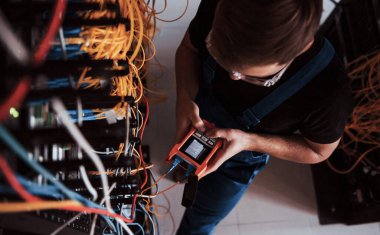 Sunucu odasında internet ekipmanı ve kablolarla çalışan ölçüm cihazıyla üniformalı genç adamın en iyi görüntüsü.