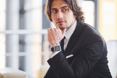 Kanepede oturuyor. Siyah takım elbiseli ve kravatlı yakışıklı iş adamının portresi..