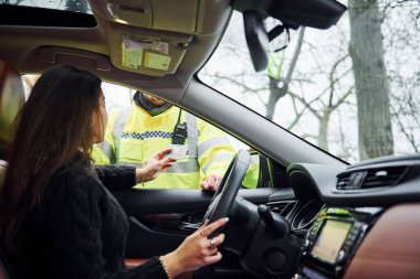 Yeşil üniformalı erkek polis yolda aracı kontrol ediyor. Rüşvet vermeye çalışan kadın.