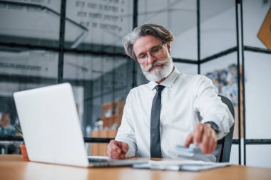 Gri saçlı, sakallı, resmi giyinmiş, elinde para tutan olgun bir iş adamı..