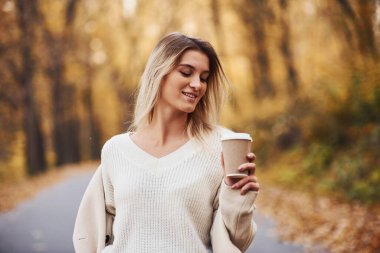 Bir bardak içki tutuyor. Gündüz vakti sonbahar ormanındaki genç esmerin portresi..