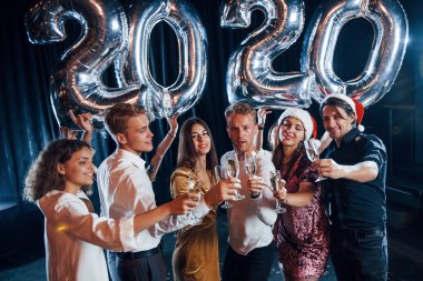 Kapı çalan gözlükler. 2020 yılını kutlamak için ellerinde balonlar ve içkilerle neşeli bir grup insan.