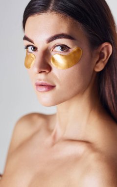 Çıplak kadın stüdyoda beyaz arka planda altın kasetlerle göz göze geliyor..