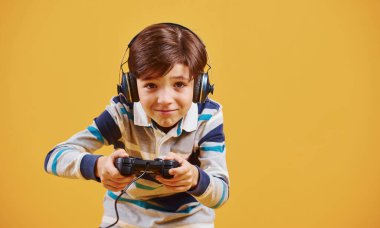 Stüdyoda sarı arka planda video oyunu oynayan sevimli küçük çocuk..