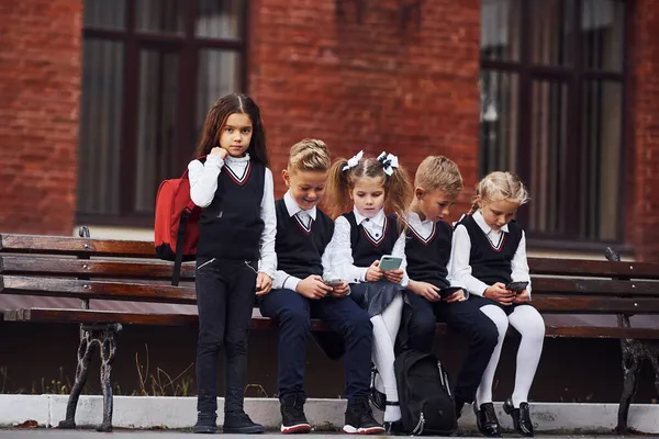 Grupo Crianças Uniforme Escolar Senta Banco Livre Juntos Perto Edifício — Fotografia de Stock