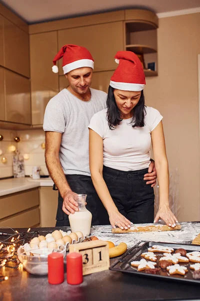 キッチンにサンタの帽子が一緒に屋内に立っているカップル — ストック写真