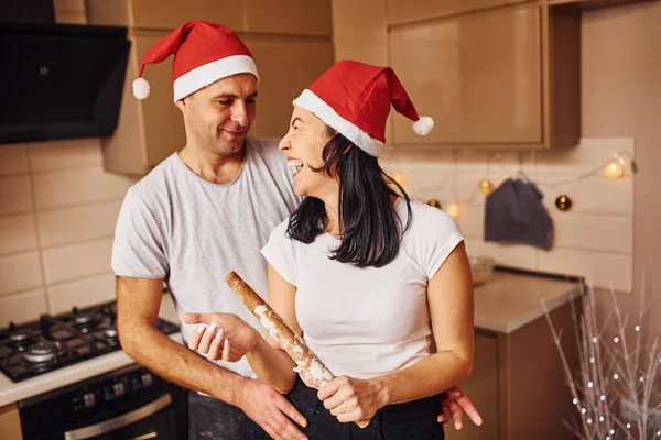 キッチンにサンタの帽子が一緒に屋内に立っているカップル — ストック写真