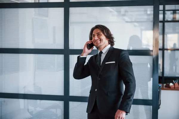 在办公室里通过电话交谈 穿着黑色西服打领带的年轻英俊商人的画像 — 图库照片