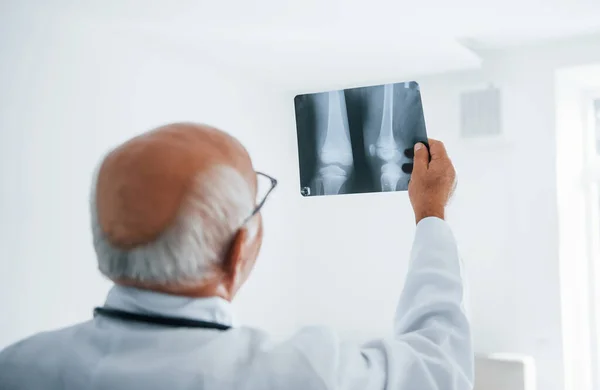 Beyaz Üniformalı Kıdemli Doktor Insan Bacağının Röntgenini Inceliyor — Stok fotoğraf