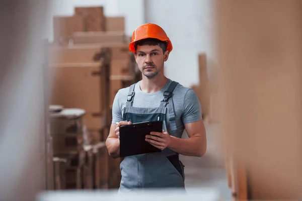 Storage worker in uniform and notepad in hands checks production.