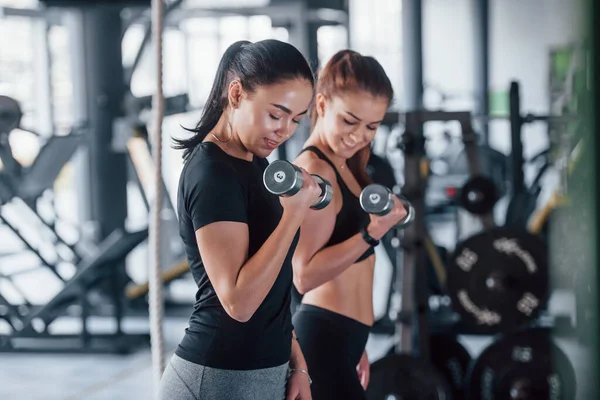 Kadın kişisel antrenör, spor salonunda egzersiz yapan kadına yardım ediyor..