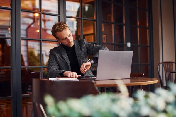 穿着正装的优雅的年轻人带着笔记本电脑坐在咖啡店里 检查时间 — 图库照片