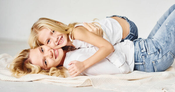 Mother with her daughter together is on the ground in the studio with white background.