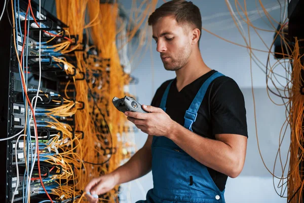 Ölçüm cihazlı üniformalı genç adam sunucu odasında internet ekipmanı ve kablolarla çalışıyor..