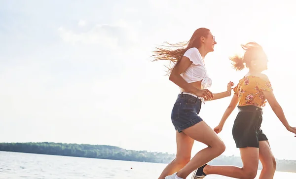 2人の女性の友人が走り 晴れた日に湖の近くのビーチで楽しんでいます — ストック写真