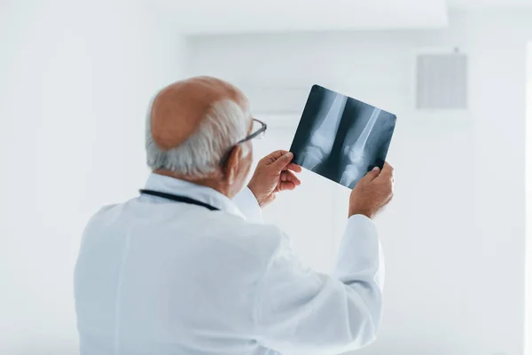 Hombre Mayor Médico Uniforme Blanco Examina Radiografía Piernas Humanas — Foto de Stock