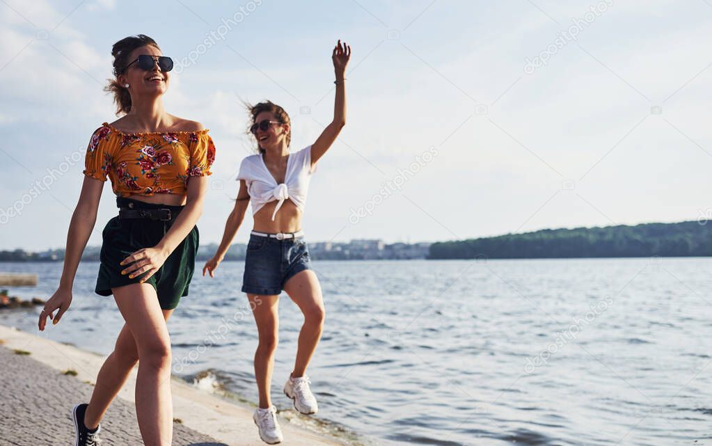 Two female friends runs and have fun at beach near the lake at sunny daytime.