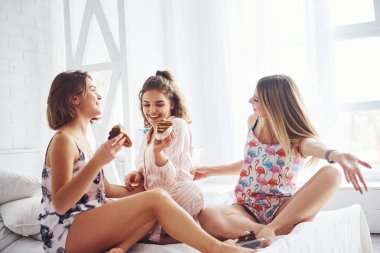 Birlikte tatlı yiyorlar. Mutlu bayan arkadaşlar yatak odasında pijama partisinde iyi vakit geçiriyorlar..