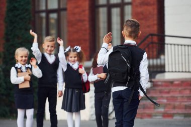 Okul üniformalı bir grup çocuk eğitim binasının yanında açık havada beraberler..